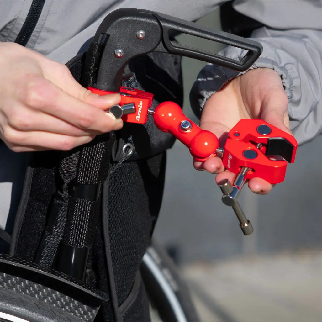 Rote Arnie Anhängerkupplung wird am Rollstuhlgriff befestigt. Praktische Lösung für den Transport von Gepäckstücken.