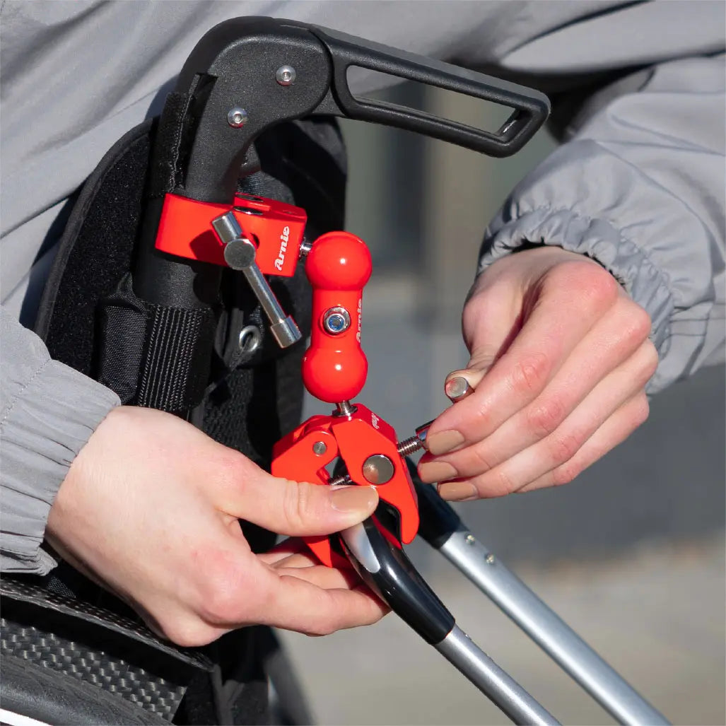 Montage der roten Arnie Anhängerkupplung am Rollstuhlgriff. Praktisches Zubehör für Koffertransport an Rollstühlen.