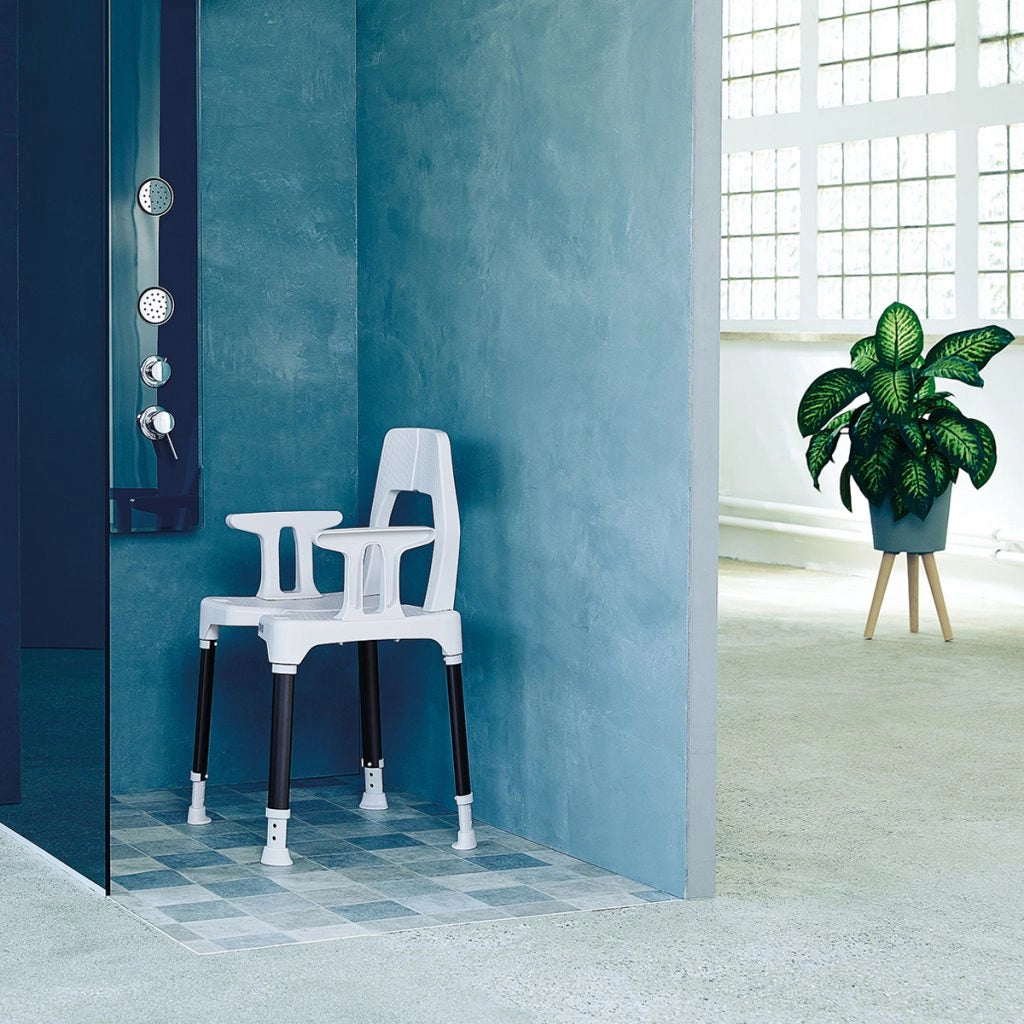 Duschstuhl TAYO B-Protect von Dietz in einer modernen, bodengleichen Dusche mit blauen Wänden – höhenverstellbar mit Rückenlehne und festen Armlehnen, platziert in einem stilvollen Badezimmer.