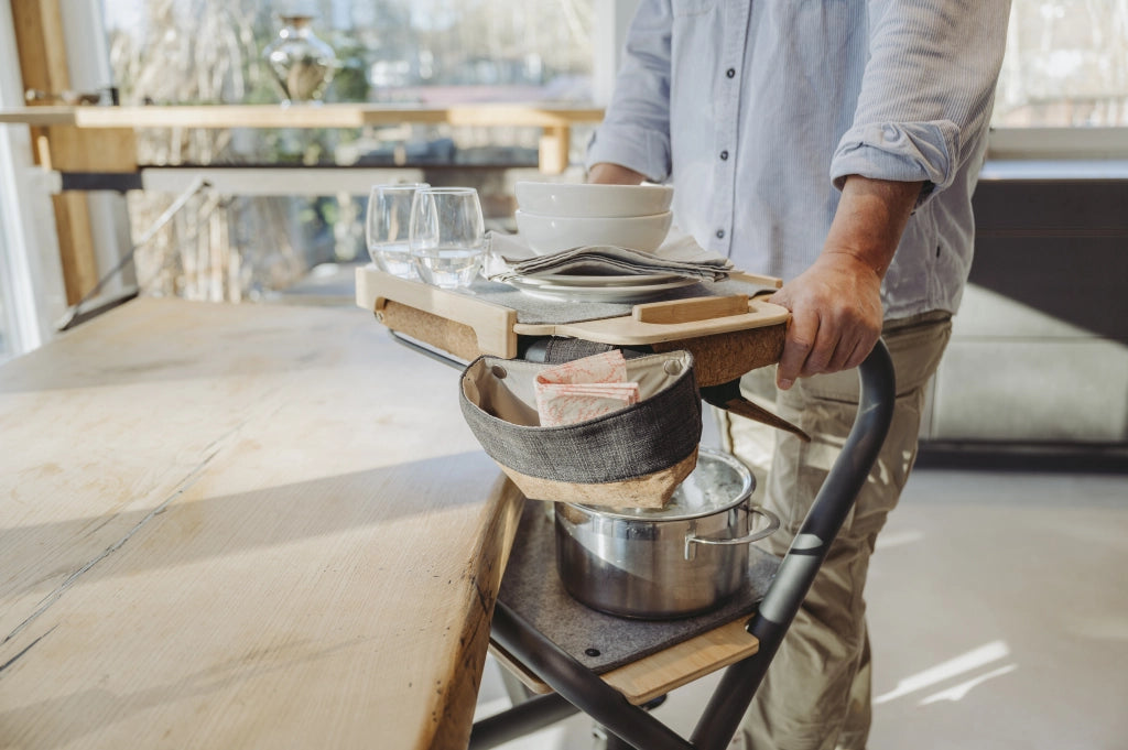 Mann transportiert Geschirr, Gläser und Kochtopf auf dem SALJOL Wohnraumrollator WR 2025 – Tablett und Sitzbrett dienen als sichere Ablage, Detailaufnahme im Alltagseinsatz