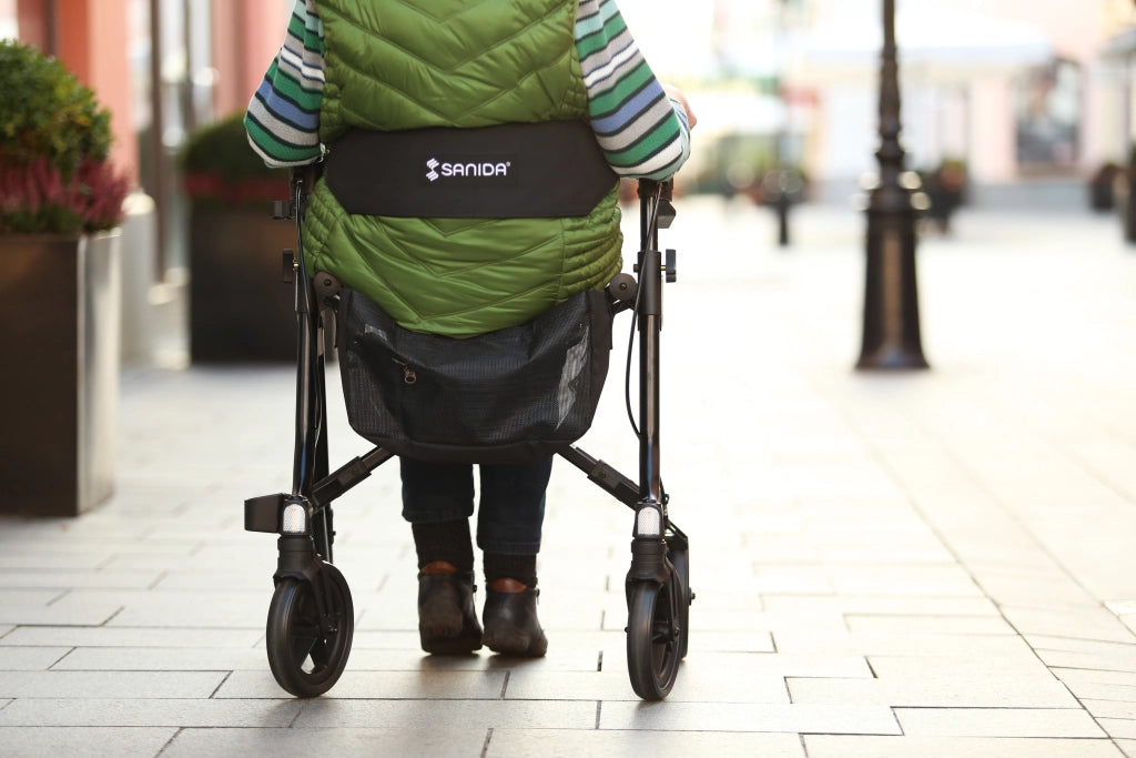 Sanida Rollator Rückansicht mit Rückengurt und einer sitzenden Frau