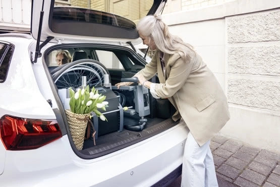 Frau lädt Alber scalamobil S45 und Rollstuhlräder platzsparend in den Kofferraum eines Autos – zeigt einfache Transportmöglichkeit der Treppensteighilfe im Alltag