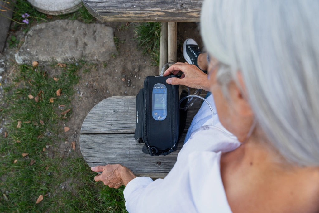 Seniorin sitzt im Freien und nutzt den tragbaren Sauerstoffkonzentrator iGo2 von Drive Medical – perfekt für mobile Sauerstofftherapie unterwegs.