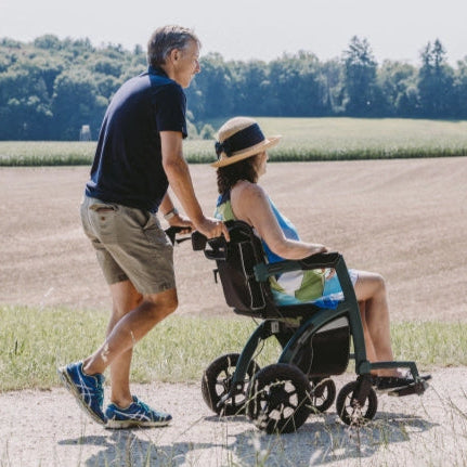 Paar spaziert durch ländliche Landschaft – Frau sitzt im Rollz Motion 2.1 Rollstuhl, der von ihrem Partner geschoben wird.