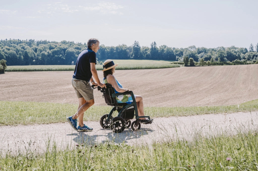Paar spaziert durch ländliche Landschaft – Frau sitzt im Rollz Motion 2.1 Rollstuhl, der von ihrem Partner geschoben wird.