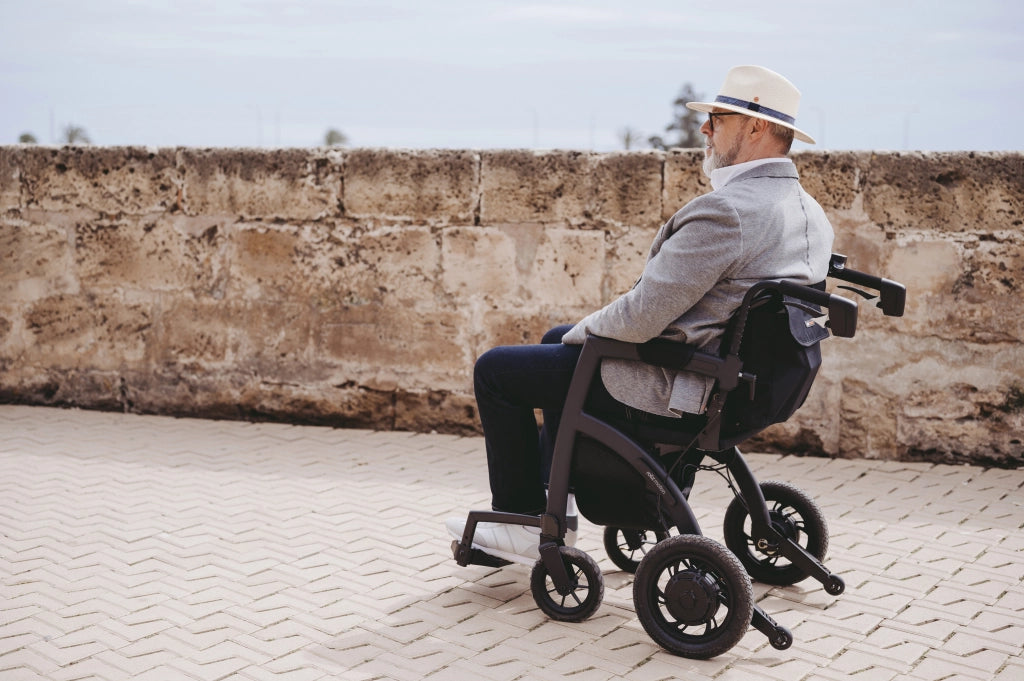 Älterer Mann mit Hut fährt entspannt im Rollz Motion Electric entlang einer historischen Steinmauer. Der innovative 3-in-1-Rollator und Elektrorollstuhl bietet komfortable Mobilität für den Außenbereich.